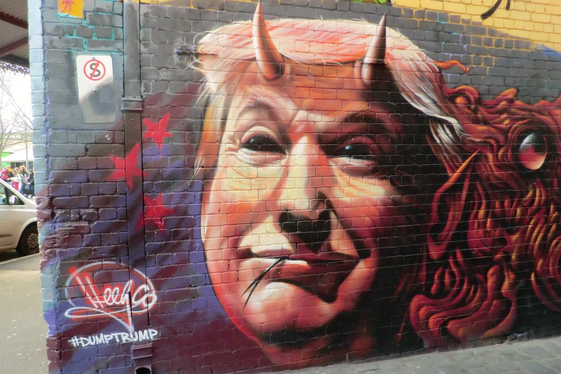 Graffiti mural depicting Donald Trump with devil horns and a mischievous expression, tagged with "#DumpTrump" and artist signature.